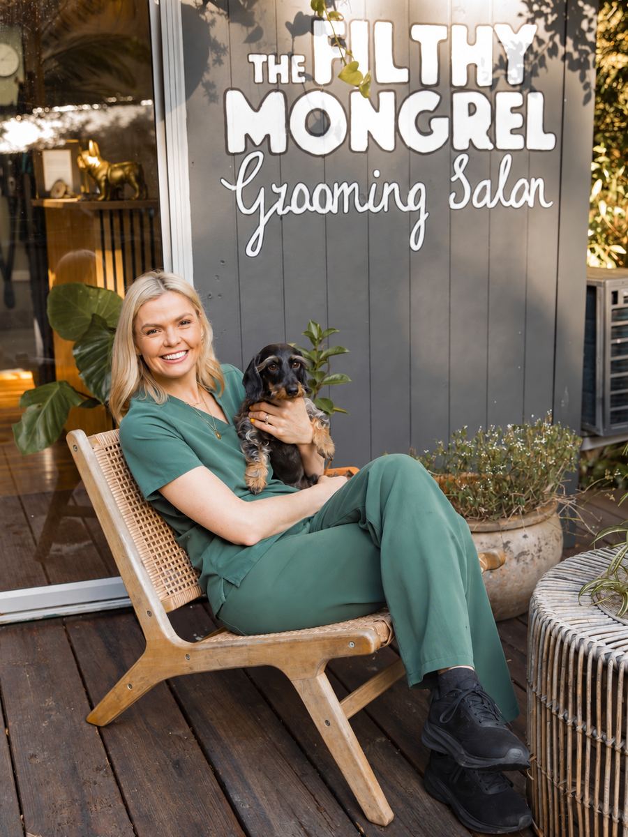 Amy sitting outside The Filthy Mongrel salon with a wire-haired dachshund on her lap