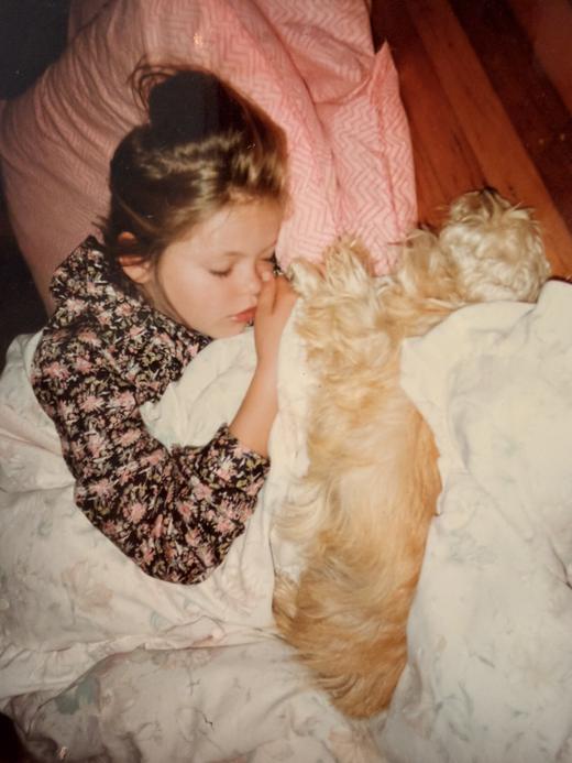 Young Amy asleep in bed curled up with Blossom, a fluffy golden dog