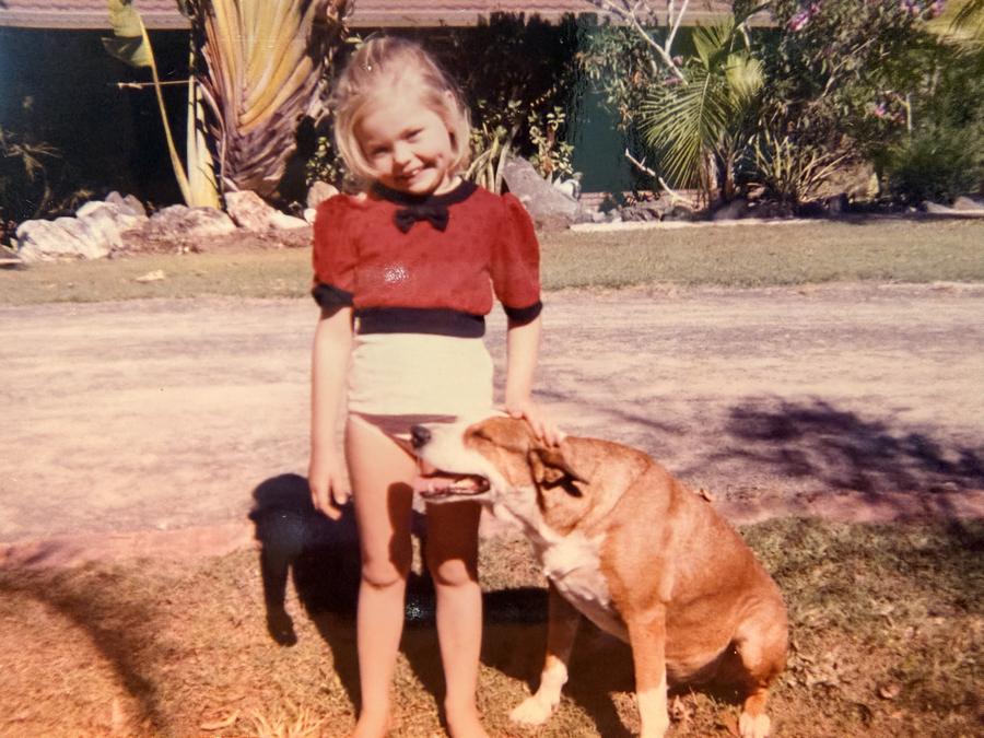 Young Amy in a red top smiling with her hand on the head of Faithful, a big tan dog